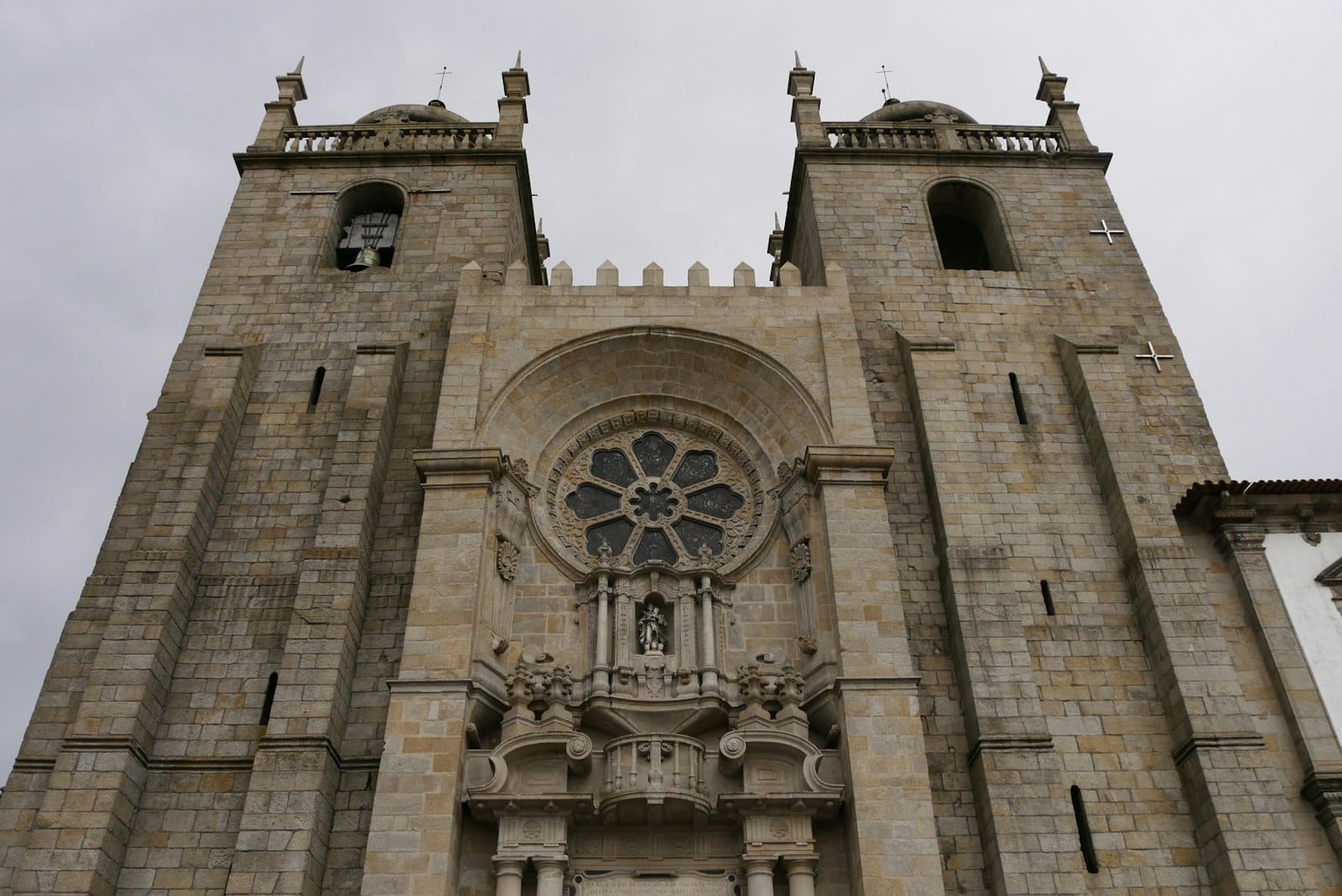 La maestosa facciata in pietra della Cattedrale di Porto con torri gemelle, ingresso ad arco e un elaborato rosone sotto un cielo nuvoloso.