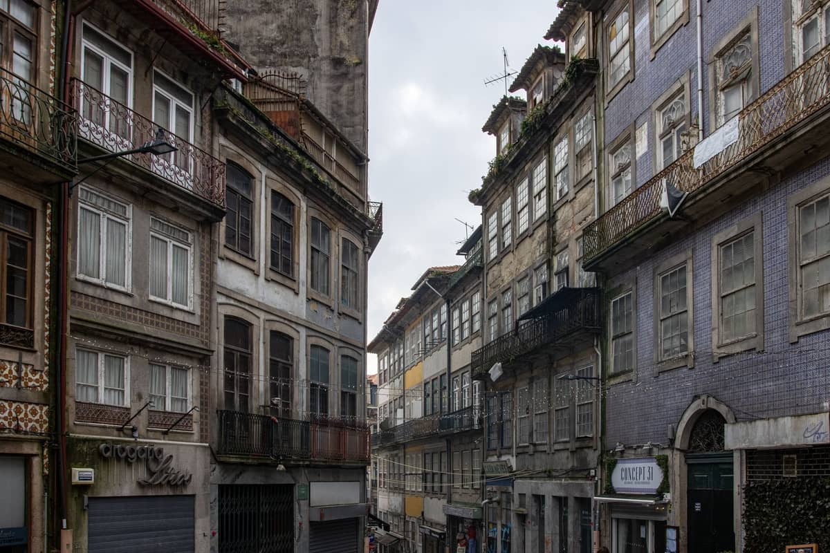Une classique rue étroite de Porto bordée de bâtiments historiques à plusieurs étages, dont beaucoup sont ornés d'azulejos et de balcons en fer forgé, reflétant un contexte architectural authentique.