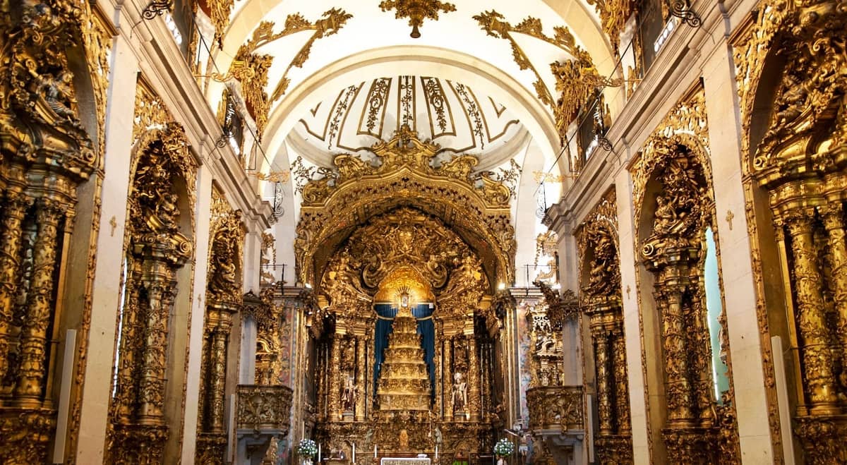 Intérieur d'église somptueusement décoré à Porto avec des sculptures en bois baroques dorées et un retable doré orné sous de hautes arches blanches.