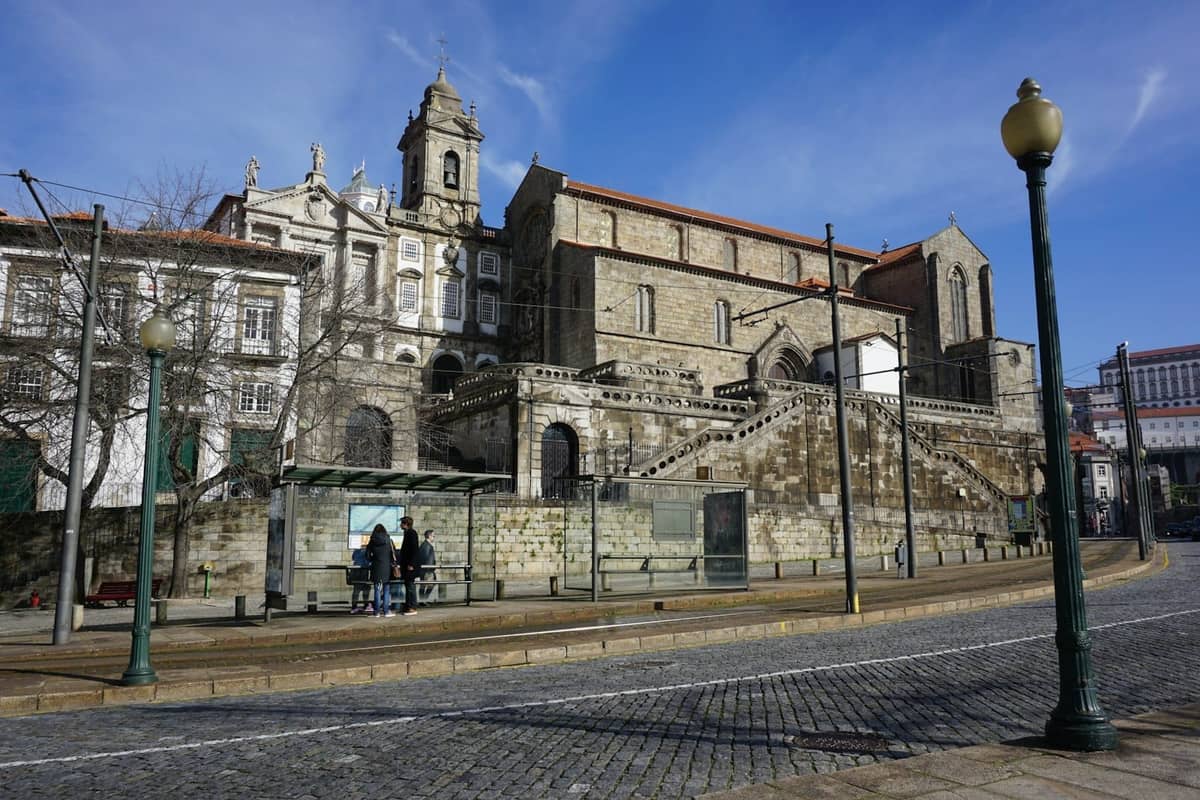 Vue large de la Cathédrale de Porto avec ses murs de pierre médiévaux et son escalier, au-dessus de la rue par une journée ensoleillée.