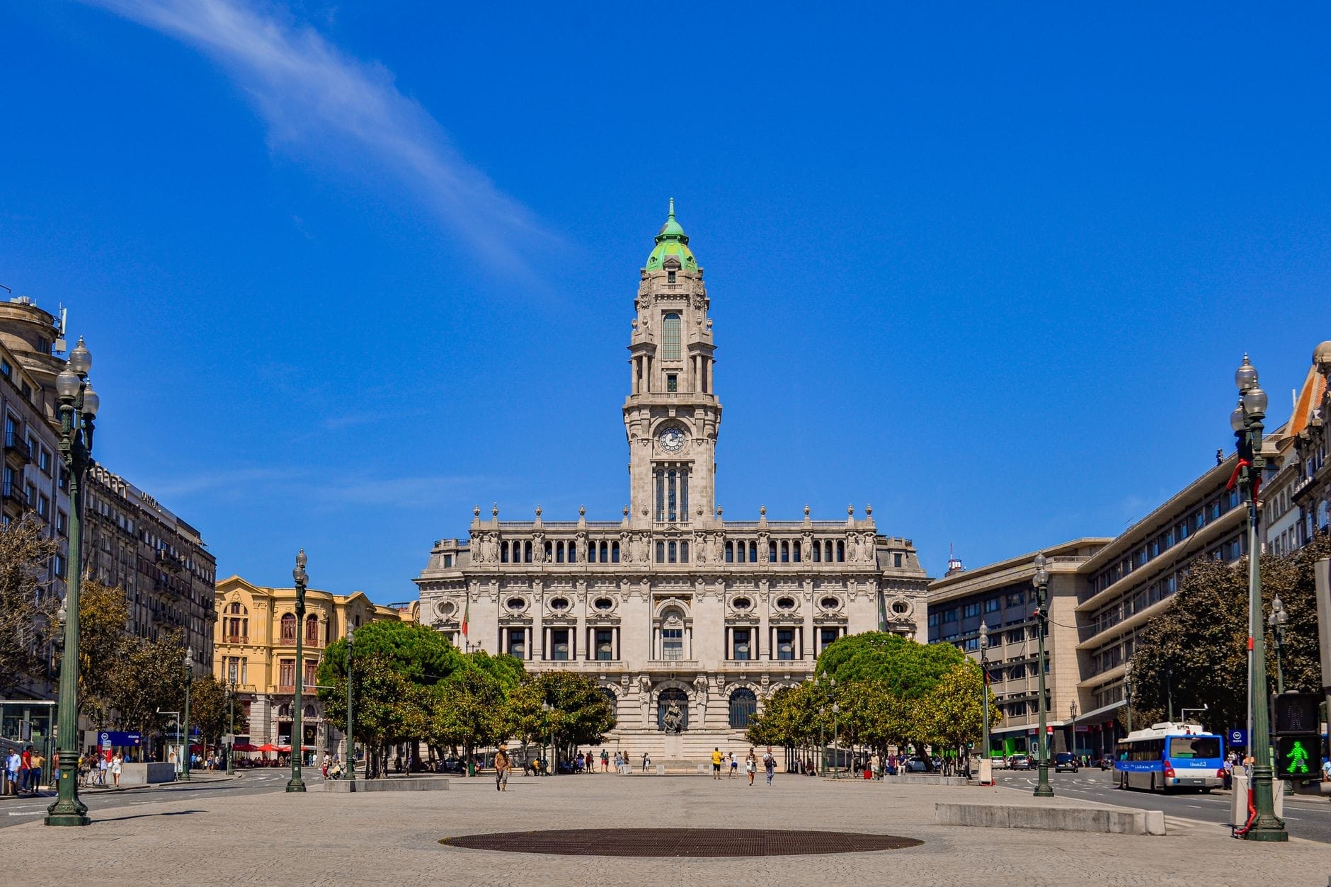 Il Municipio di Porto con il suo campanile inquadrato dall'Avenida dos Aliados, fotografato in una giornata limpida con cielo azzurro e persone nella piazza.