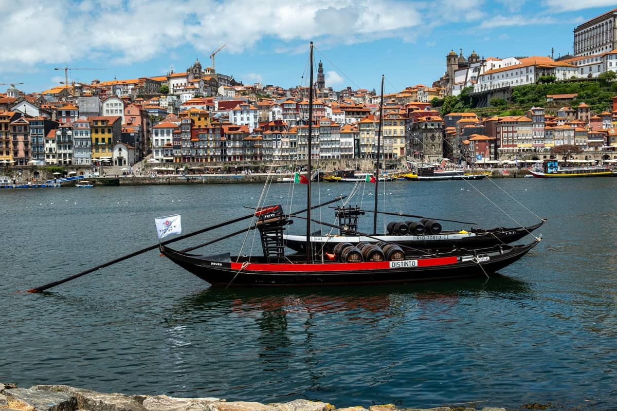 Bateau traditionnel de vin de Porto avec des tonneaux sur le fleuve Douro, panorama urbain et berges de Porto en arrière-plan sous ciel bleu