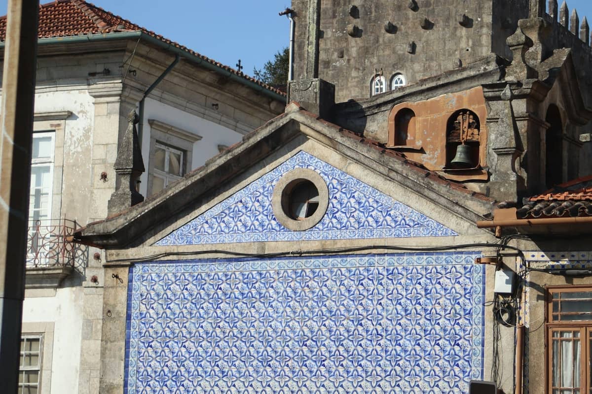 Facciata di un edificio di Porto decorata con intricati azulejos blu e bianchi, adiacente a strutture in pietra più antiche.