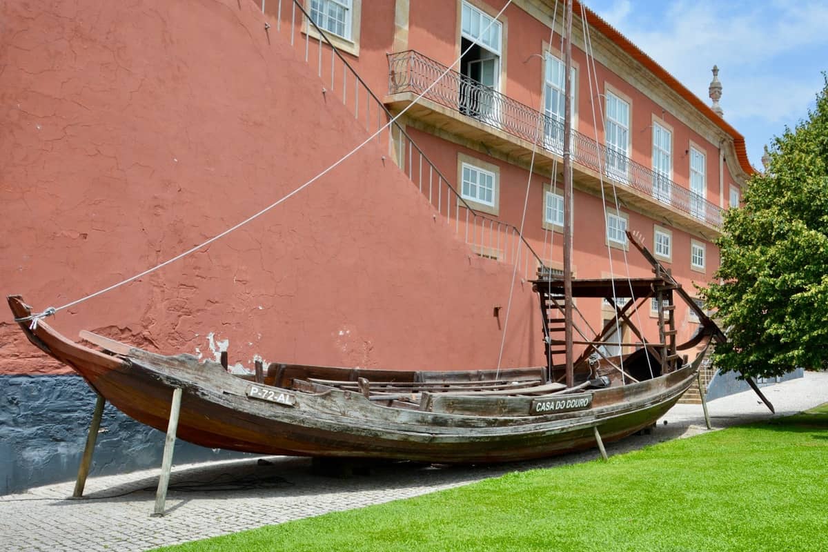Tradizionale barca in legno esposta all'esterno di un edificio museale dalle pareti rosse a Porto, Portogallo, in una giornata di sole.