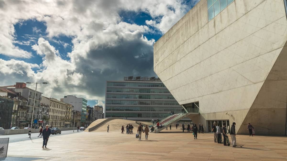 Edificio architettonico moderno a Porto con persone che camminano in una grande piazza aperta sotto un cielo spettacolare.
