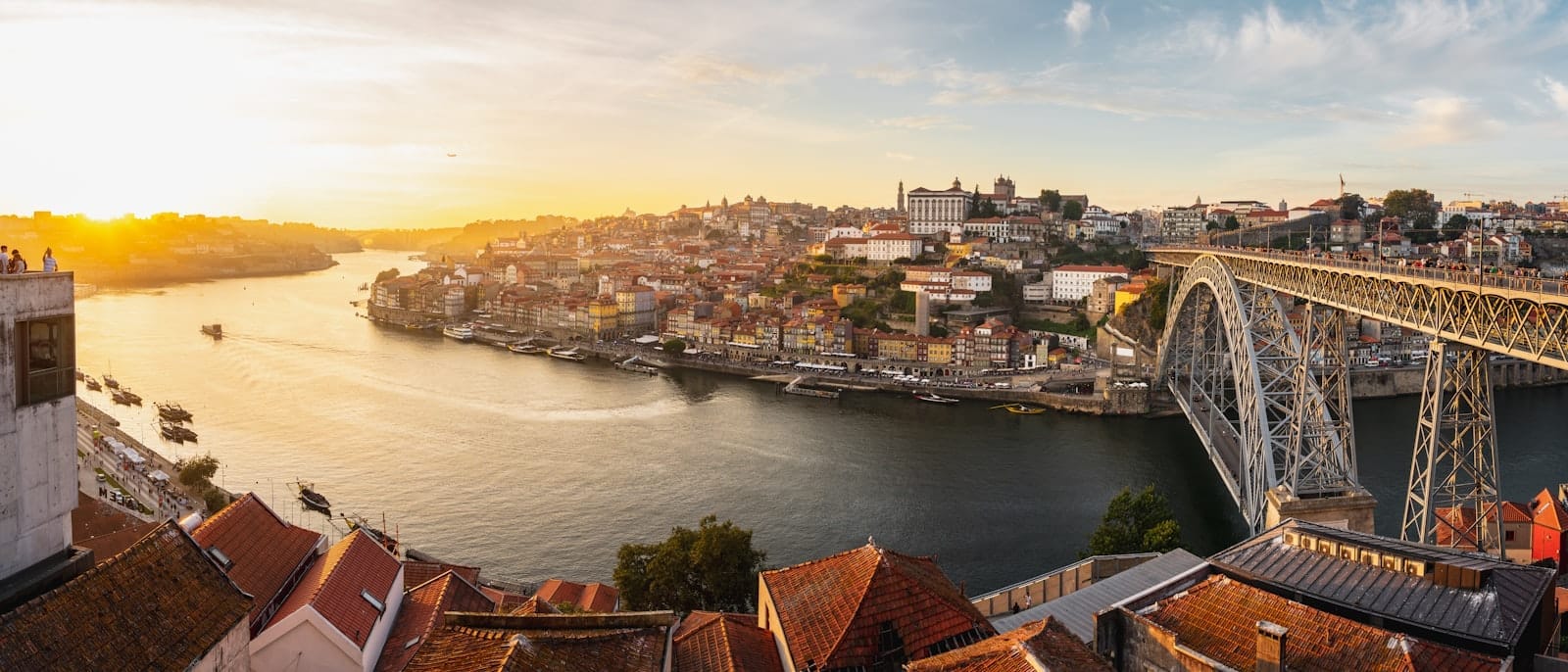 Vista panorâmica do Porto ao pôr do sol com o Rio Douro, os coloridos prédios da Ribeira e a Ponte Dom Luís I banhados pela luz dourada.