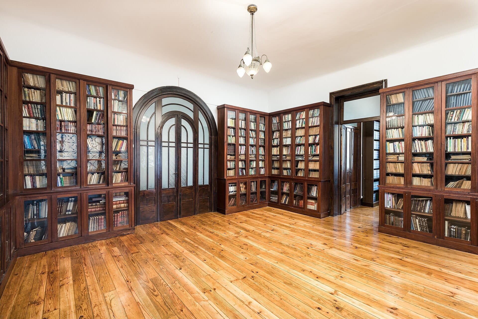 Sala spaziosa e ben illuminata all'interno del Porto Jewish Museum con librerie in legno piene di libri, pavimenti in legno lucidato e porte ad arco con pannelli in vetro.