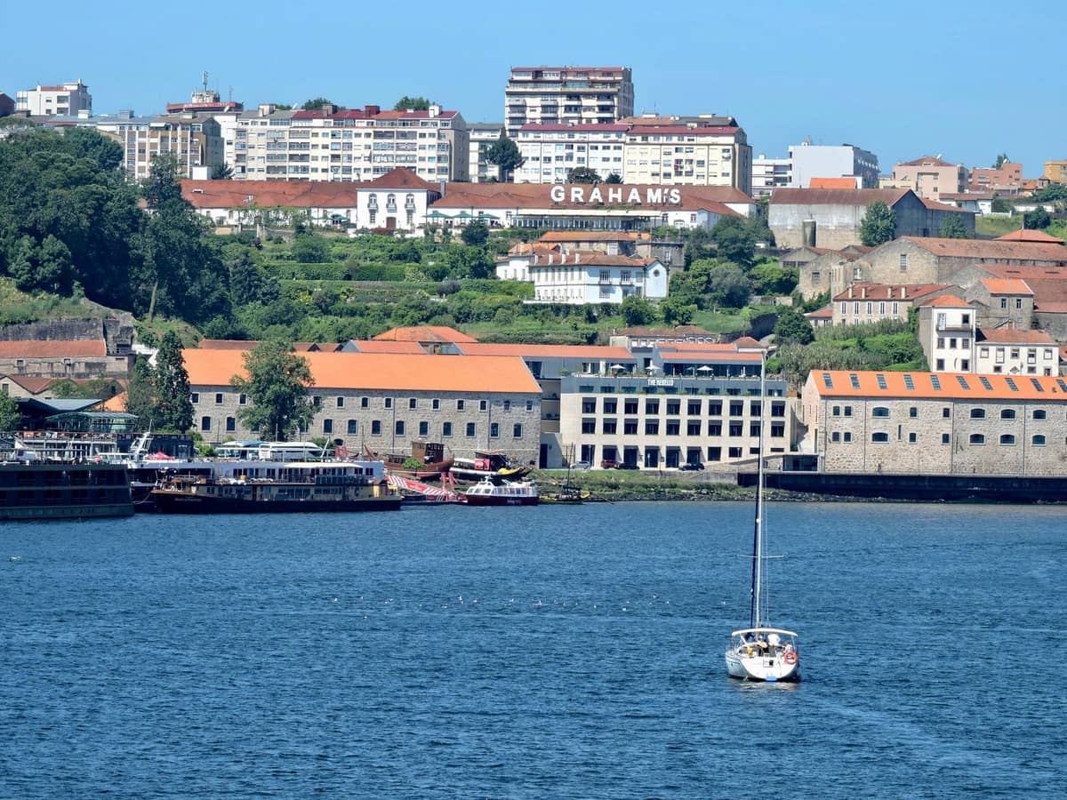 Vista sul fiume Douro a Porto, con storiche cantine di vino di Porto e una barca a vela in primo piano, insegna di Graham's visibile sulla collina.