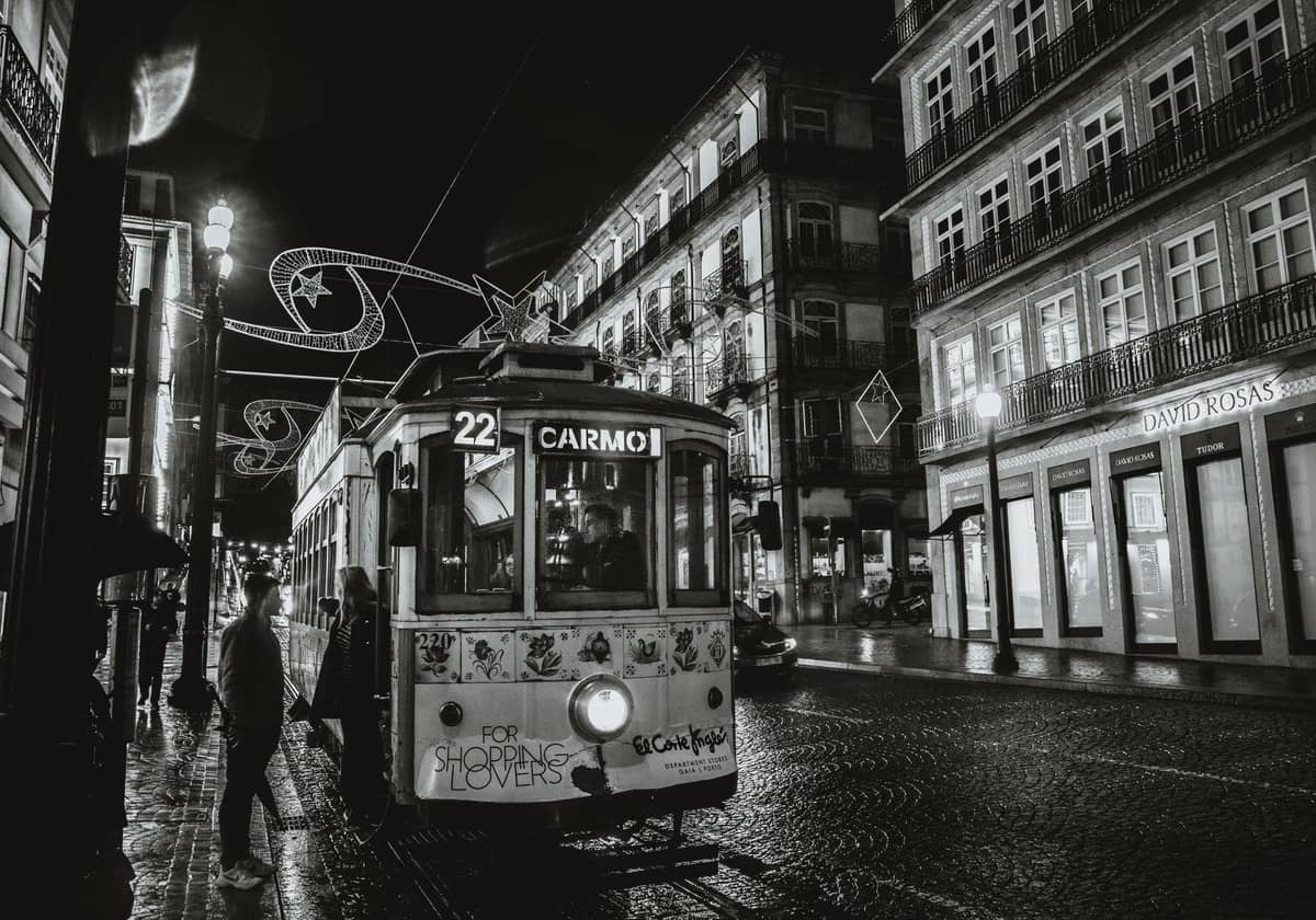 Portekiz'in Porto şehrinde gece sokak sahnesi, '22 Carmo' yazılı klasik bir tramvay, tarihi binalar ve aydınlatılmış gece hayatı atmosferi.