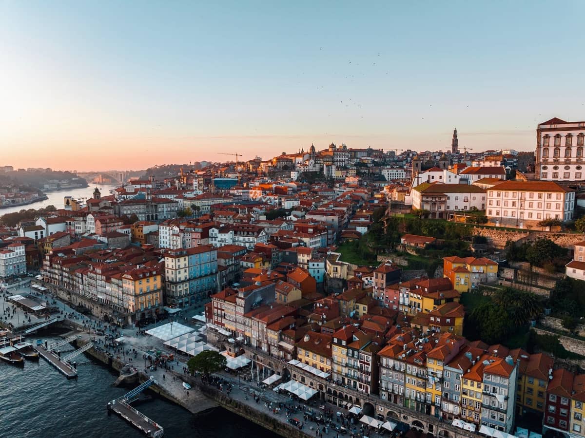 Colorati edifici tradizionali sul lungofiume e vivace passeggiata lungo il fiume Douro a Porto al tramonto, che mostrano il centro storico compatto e vivace della città.