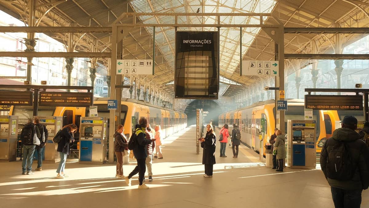 Persone che usano le biglietterie automatiche e salgono su treni pendolari gialli alla stazione ferroviaria di São Bento a Porto, in Portogallo, con la luce del sole che filtra nella storica stazione.