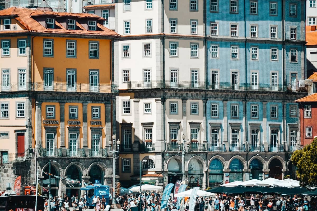 Belebte Sommermenge im historischen Ribeira-Viertel in Porto, mit bunten alten Gebäuden, Straßencafés und voll besetzten Außenbereichen, die die Hochsaison des Tourismus veranschaulichen.