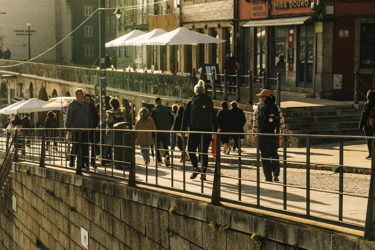Menschen, die entlang der lebhaften Uferpromenade in Porto spazieren, mit historischen Gebäuden und Straßencafés im Hintergrund.