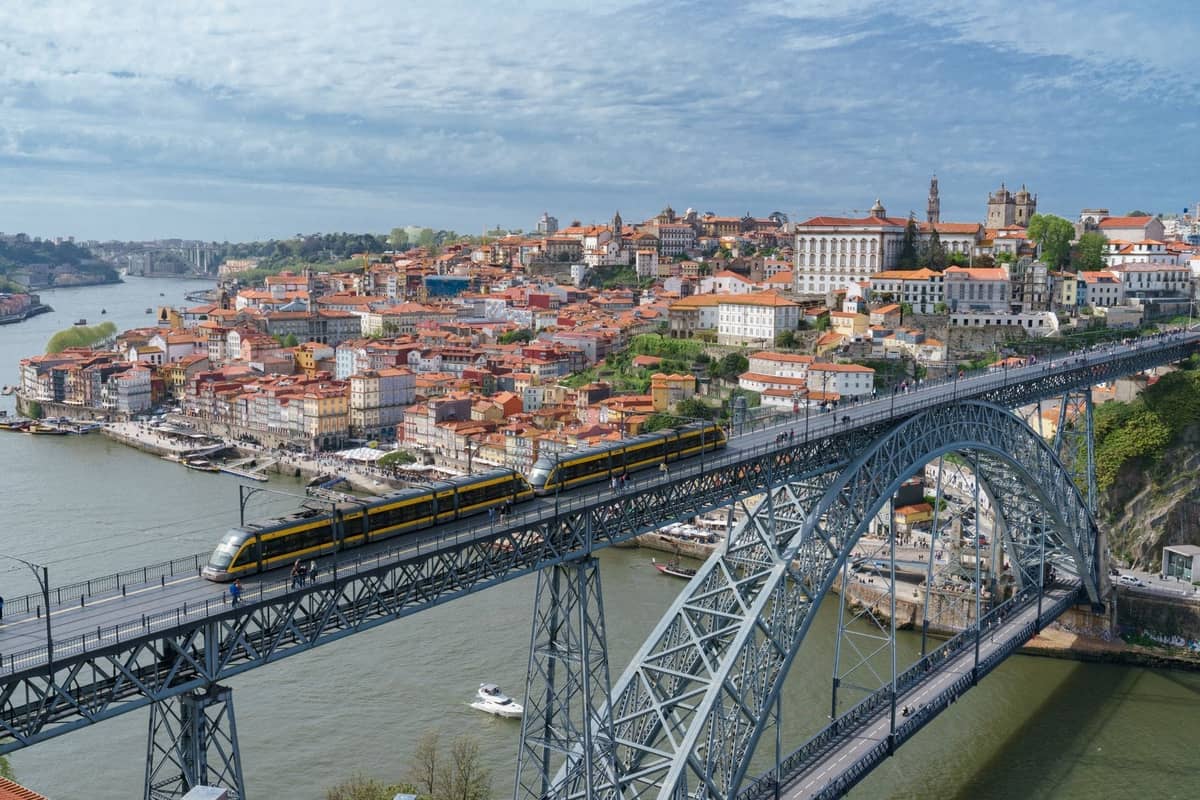Weiter Blick auf Porto mit der ikonischen Dom-Luís-I-Brücke über den Fluss Douro und historischen Stadtgebäuden im Hintergrund.