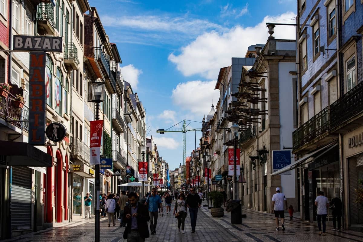 Belebte Einkaufsstraße in Porto mit bunten traditionellen Gebäuden, Geschäften und Menschen, die unter einem strahlend blauen Himmel spazieren.