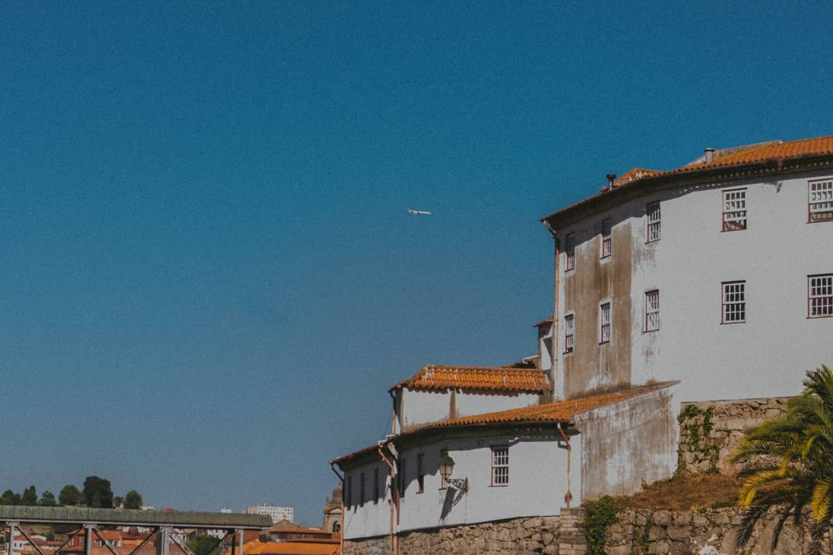 Edifici tradizionali di Porto con un aereo che vola sopra, cielo azzurro e un ponte sullo sfondo.