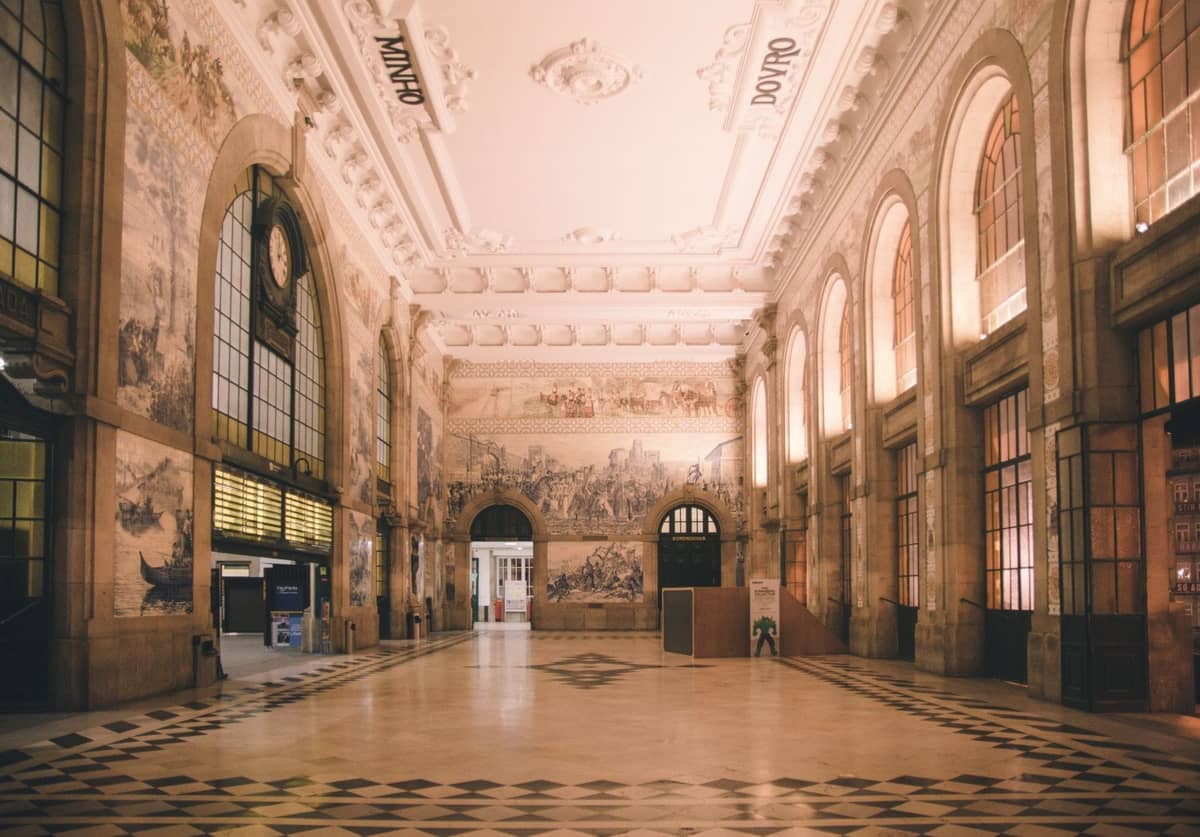 Vista ampia della sala principale della stazione ferroviaria di São Bento a Porto con grandi finestre ad arco, soffitto ornato e famosi murales di piastrelle azulejo blu.