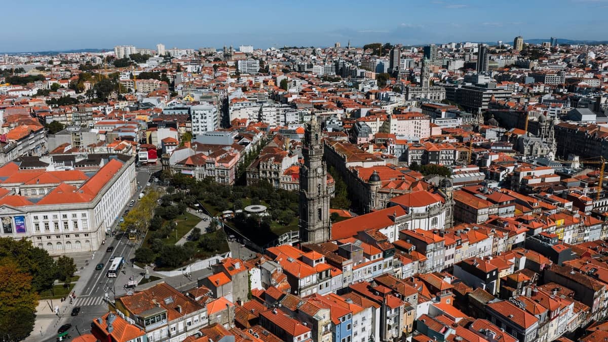 Vista aérea de Oporto mostrando el denso centro histórico con la icónica Torre dos Clérigos, tejados de tejas y calles compactas transitables bajo un cielo azul despejado.