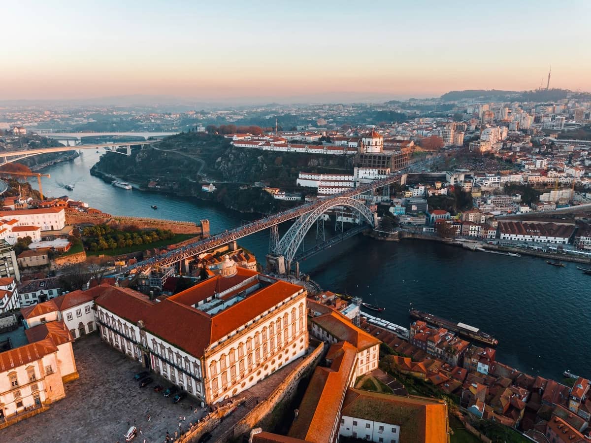 Luftaufnahme von Porto mit der Brücke Dom Luís I, dem Fluss Douro, historischen Gebäuden und dem Kloster Serra do Pilar bei Sonnenaufgang.