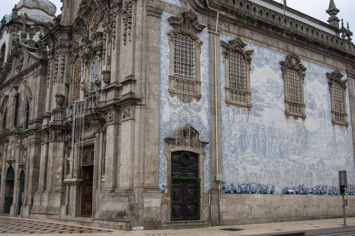 Historische Barockkirche in Porto mit einer aufwendigen Fassade und einem großen blau-weißen Azulejo-Kachelmosaik, von der Straßenecke aus gesehen.
