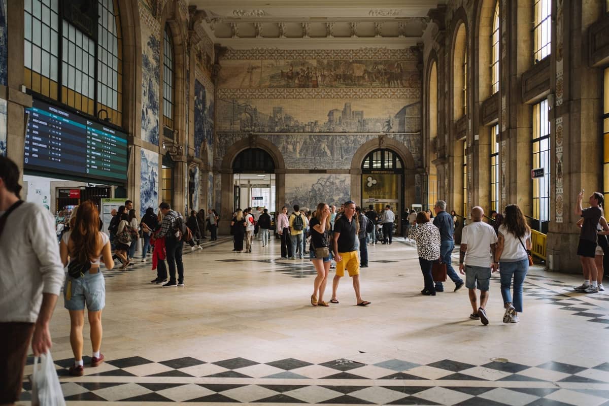 Das Innere des Bahnhofs São Bento in Porto mit Menschenmassen, Azulejo-Kachelmuralen, hohen Bogenfenstern und einem gemusterten Boden.