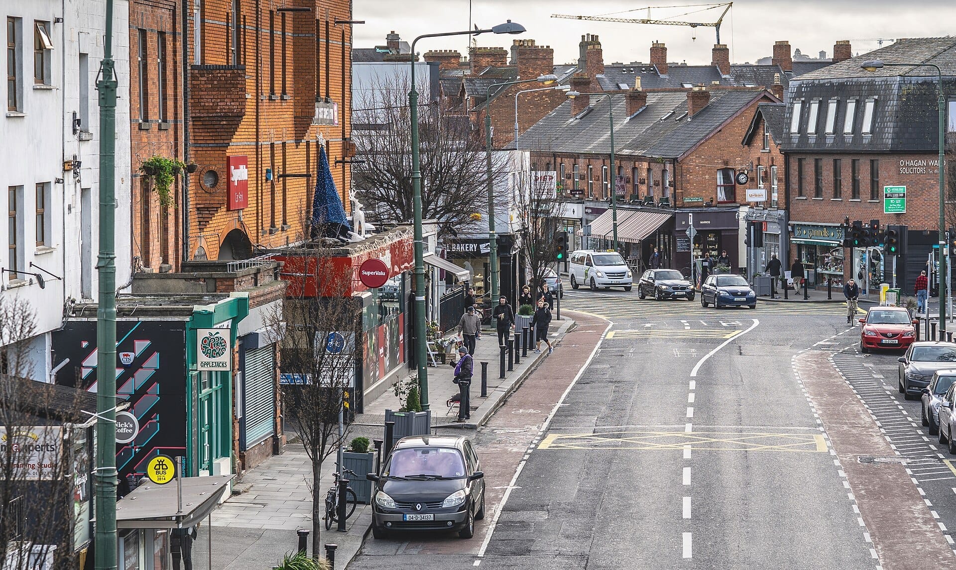 วิวถนน Ranelagh ในเมือง Dublin พร้อมอาคารอิฐสีแดง ร้านค้าท้องถิ่น รถยนต์จอดอยู่ และผู้คนเดินในวันที่มีเมฆมาก