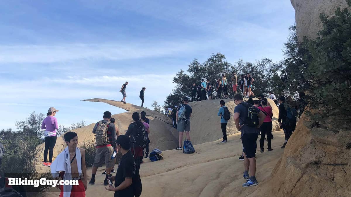 Menschengruppe am und auf dem Potato Chip Rock – dem berühmten dünnen Granitfelsen nahe dem Gipfel des Mount Woodson unter blauem Himmel.