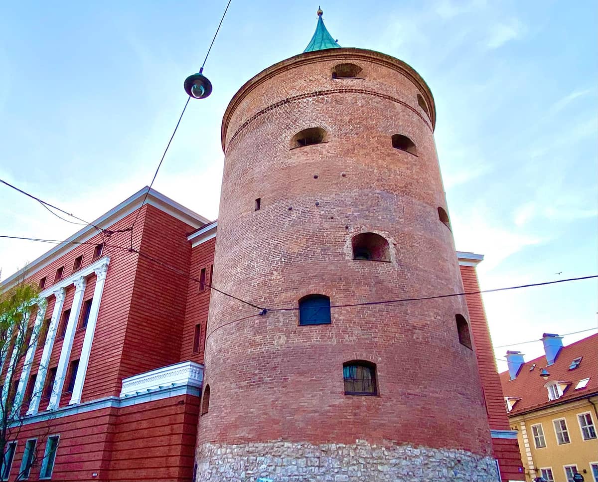 Nahaufnahme des Pulverturms in Riga – ein runder mittelalterlicher Backsteinturm, der heute das Lettische Kriegsmuseum beherbergt, vor blauem Himmel.