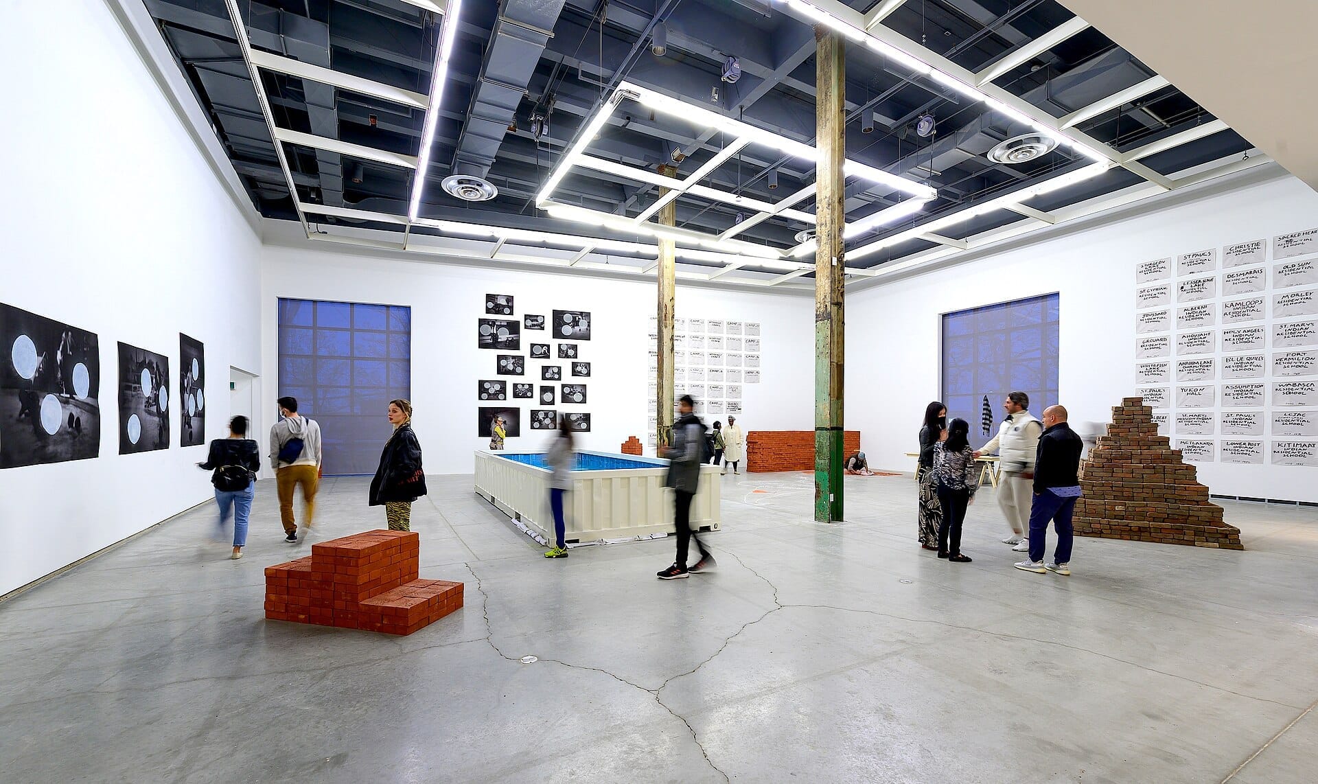 ภายใน The Power Plant Contemporary Art Gallery พร้อมผู้เข้าชมชมงานติดตั้งศิลปะสมัยใหม่ ภาพถ่ายบนผนังสีขาว และโครงเหล็กอุตสาหกรรมใต้แสงสว่างจ้า