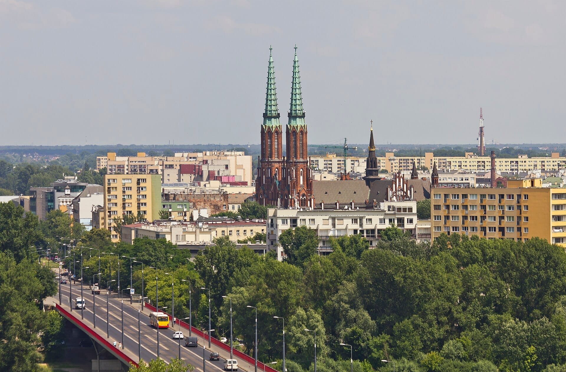 วิวย่าน Praga ในกรุง Warsaw โดดเด่นด้วยยอดแหลมคู่ของ St. Florian's Cathedral ท่ามกลางอาคารอพาร์ตเมนต์และต้นไม้เขียวขจีใต้ท้องฟ้าแจ่มใส