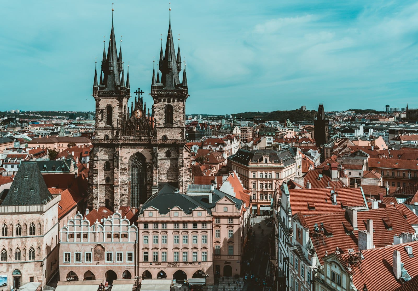Luftaufnahme der Prager Altstadt mit den gotischen Türmen der Teynkirche, umgeben von historischen Gebäuden und roten Dächern unter blauem Himmel.