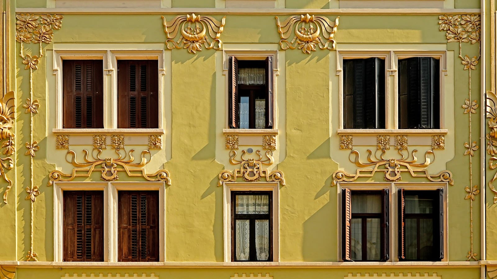 Nahaufnahme der verzierten gelben Jugendstil-Fassade eines Gebäudes in Prag mit dekorativen Stuckverzierungen und symmetrischer Fensteranordnung.