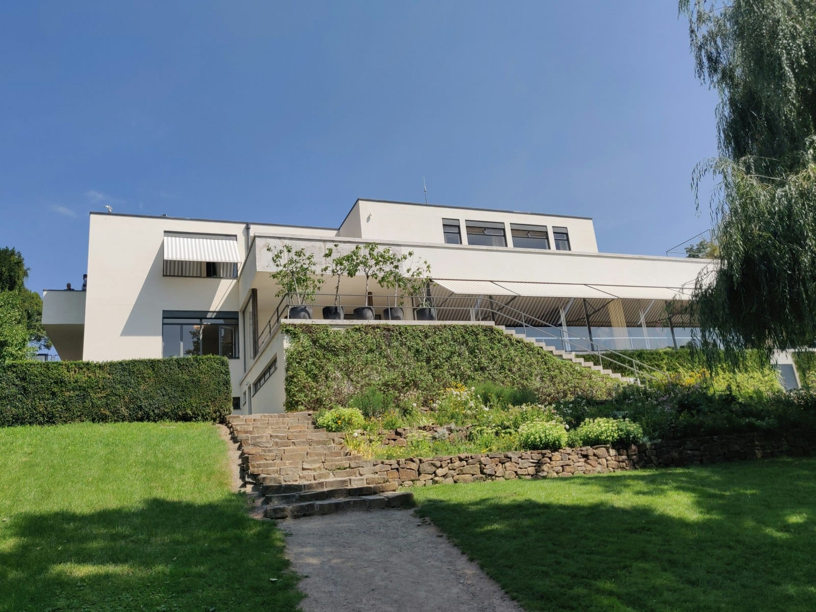 Weiße modernistische Villa mit klaren Linien und Flachdach, eingebettet in einen gepflegten Rasen unter blauem Himmel