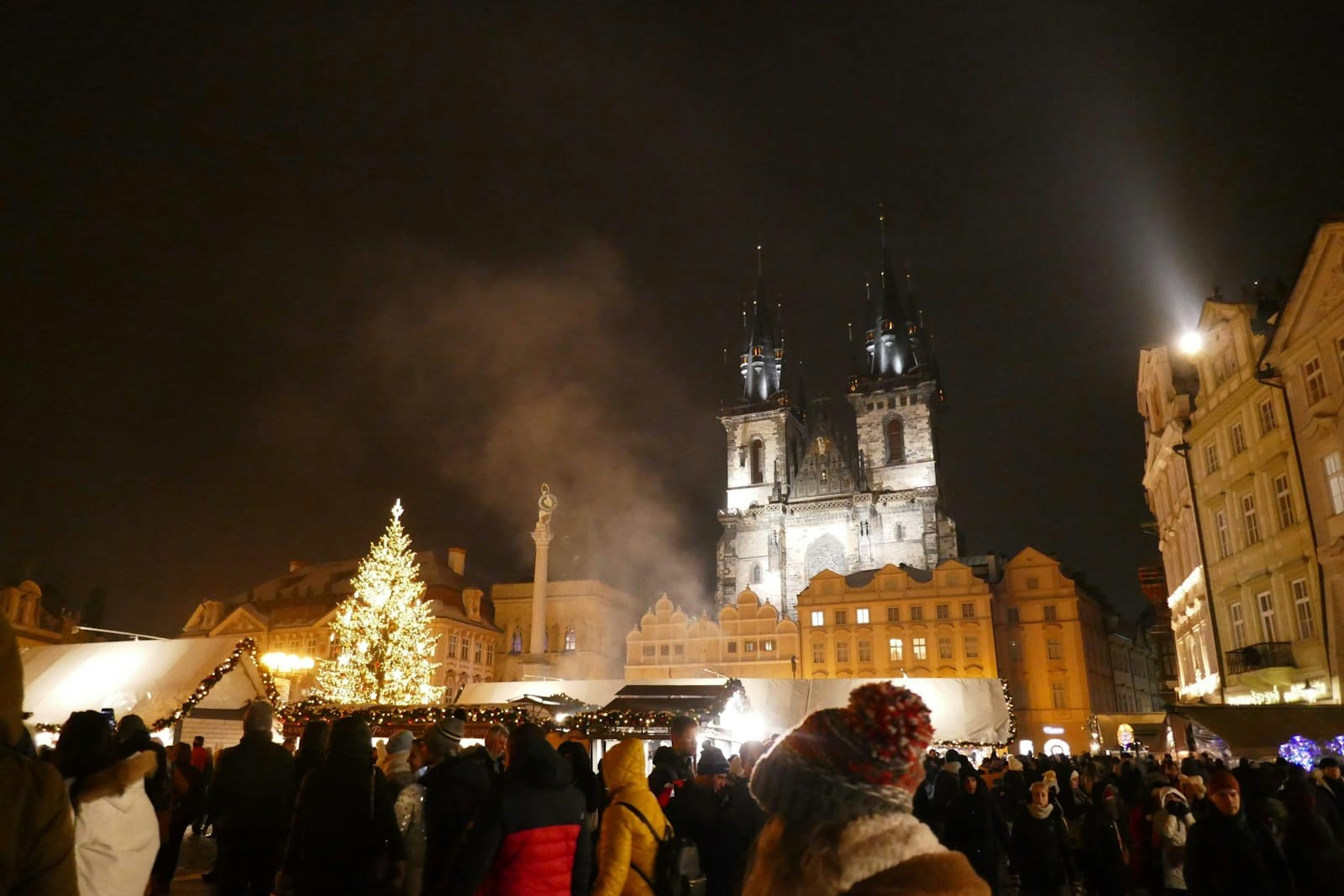 Große Menschenmenge bei Nacht auf dem Weihnachtsmarkt des Altstädter Rings in Prag, mit beleuchteten Ständen, Weihnachtsbaum und Teynkirche.