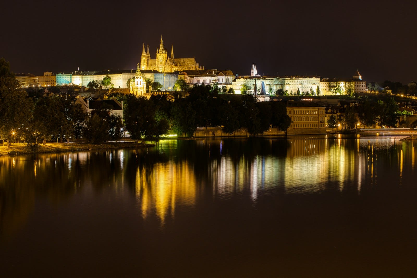 Die Prager Burg bei Nacht beleuchtet mit Spiegelungen auf der Moldau, ein romantisches Stadtbild ideal für Abendausflüge.