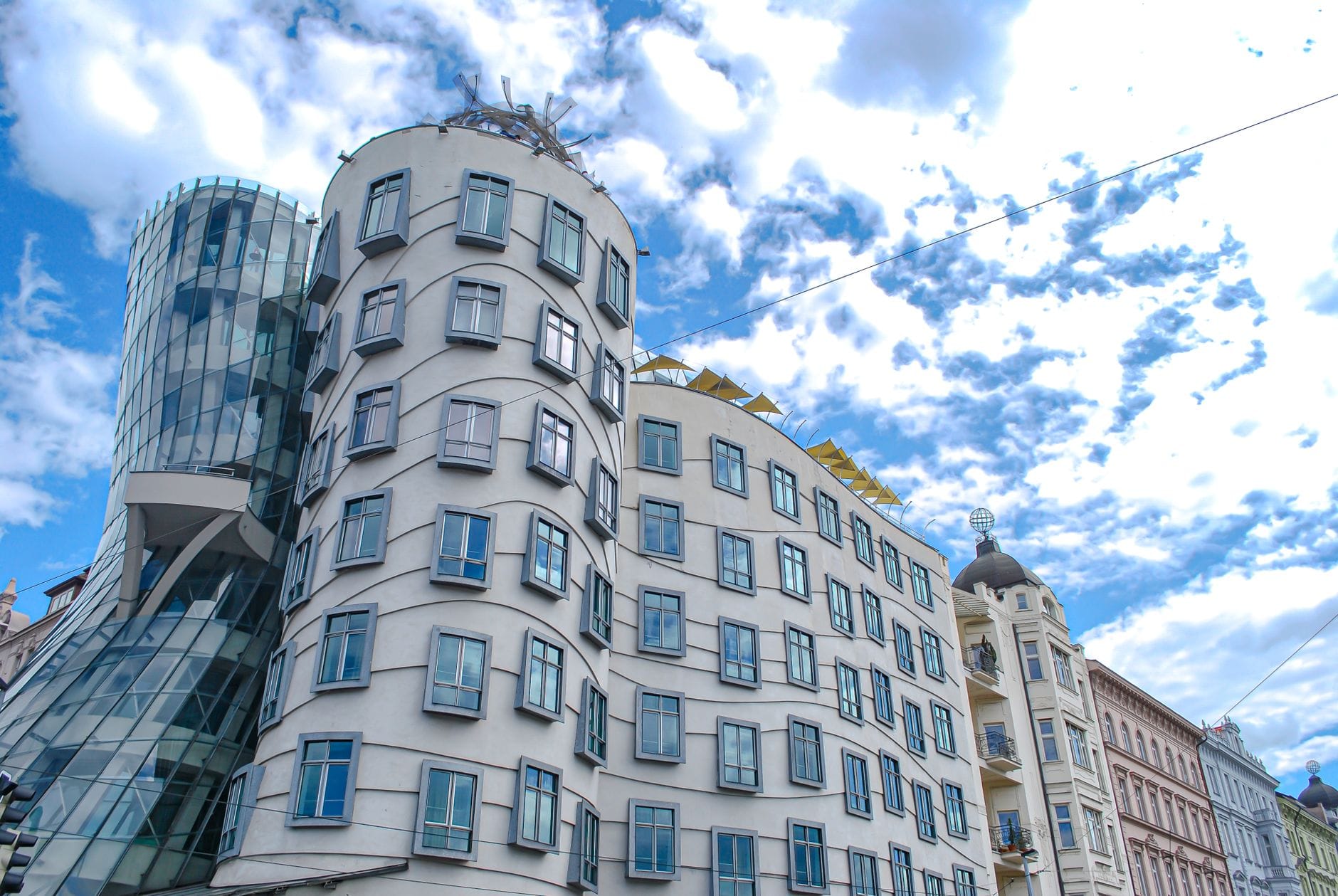 Das Tanzende Haus in Prag, ein ikonisches Beispiel moderner und ungewöhnlicher Architektur, vor einem blauen Himmel mit vereinzelten Wolken.