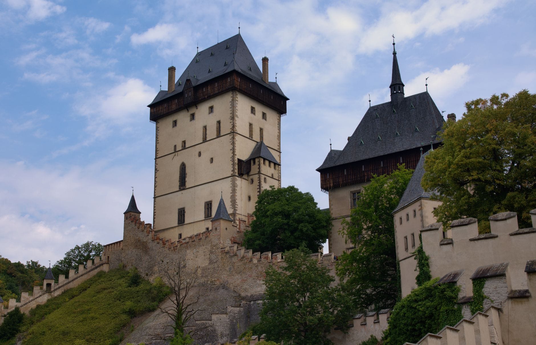 Mittelalterliche Burg auf einem Hügel mit Steinmauern und Türmen, umgeben von Bäumen unter blauem Himmel