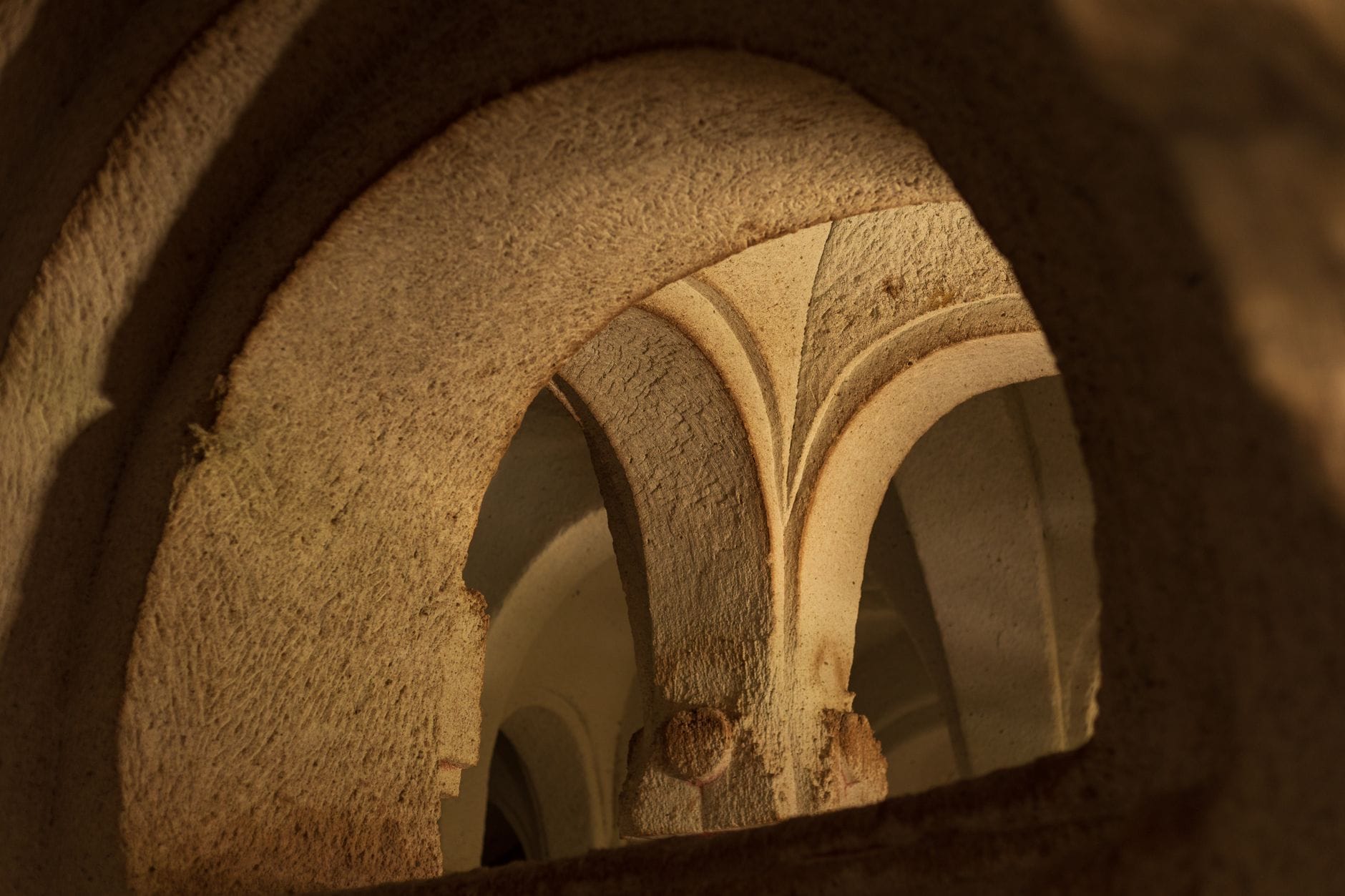Steinerne romanische Bögen und Gewölbe in einem schwach beleuchteten unterirdischen Raum, der auf Prags verborgene mittelalterliche Strukturen hindeutet.