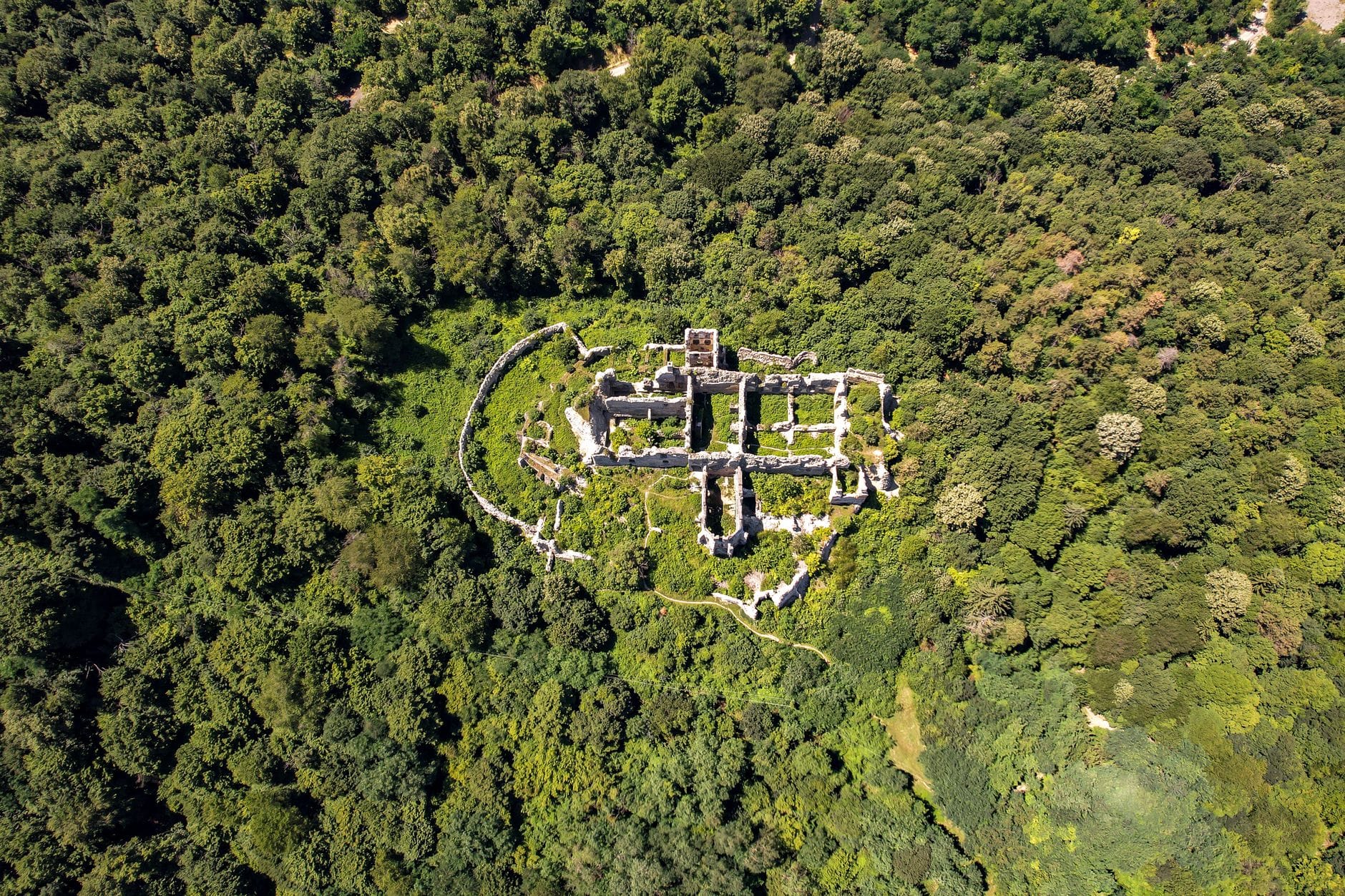 Vista aerea di antiche rovine in pietra circondate da una fitta foresta, che mostrano i resti di un antico insediamento o di una fortificazione.