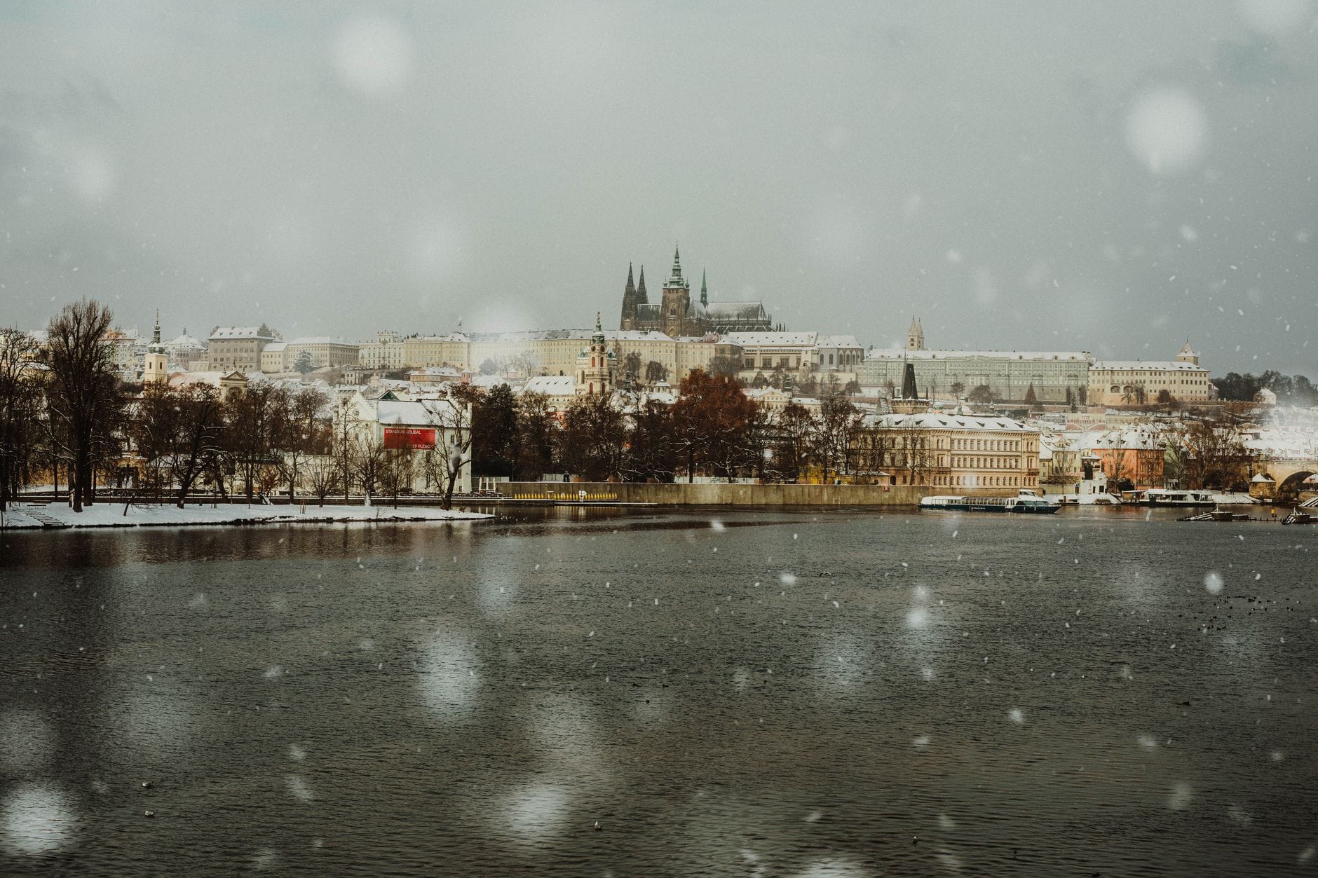 Schneefall über der Moldau mit der Prager Burg in der Ferne, das Winterwetter in Prag einfangend.