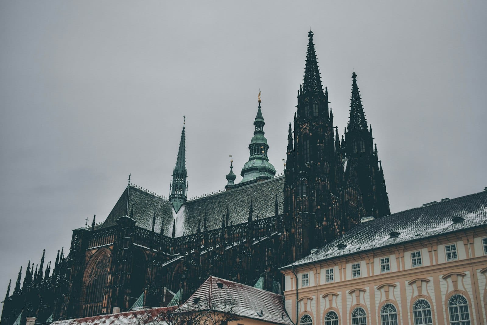 Winteransicht des Veitsdoms und der Prager Burg mit Schnee auf den Dächern und bewölktem Himmel.