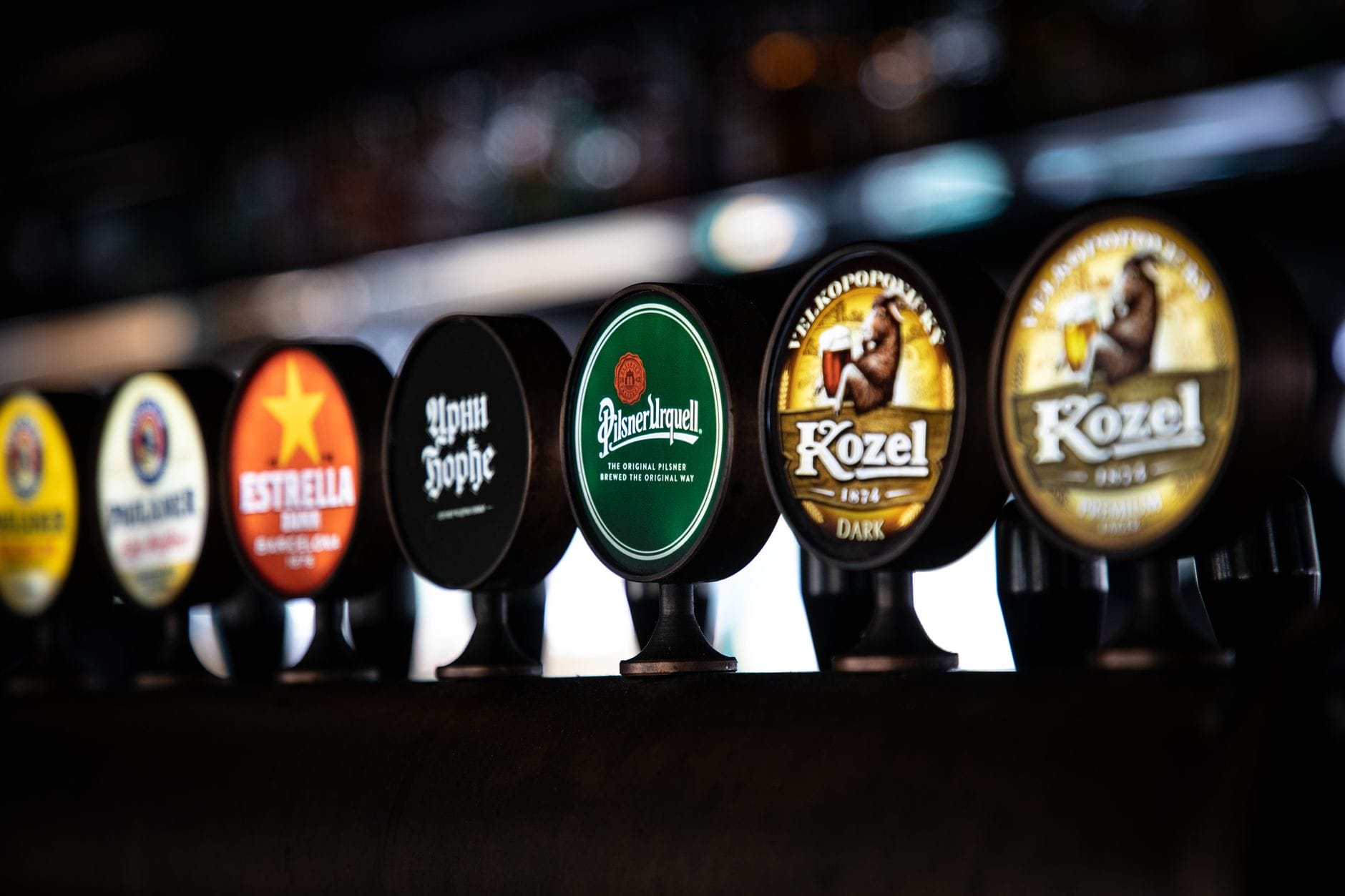 Isang hanay ng mga Czech beer tap sa isang bar sa Prague, na may mga brand tulad ng Pilsner Urquell at Kozel, na may malabong background.