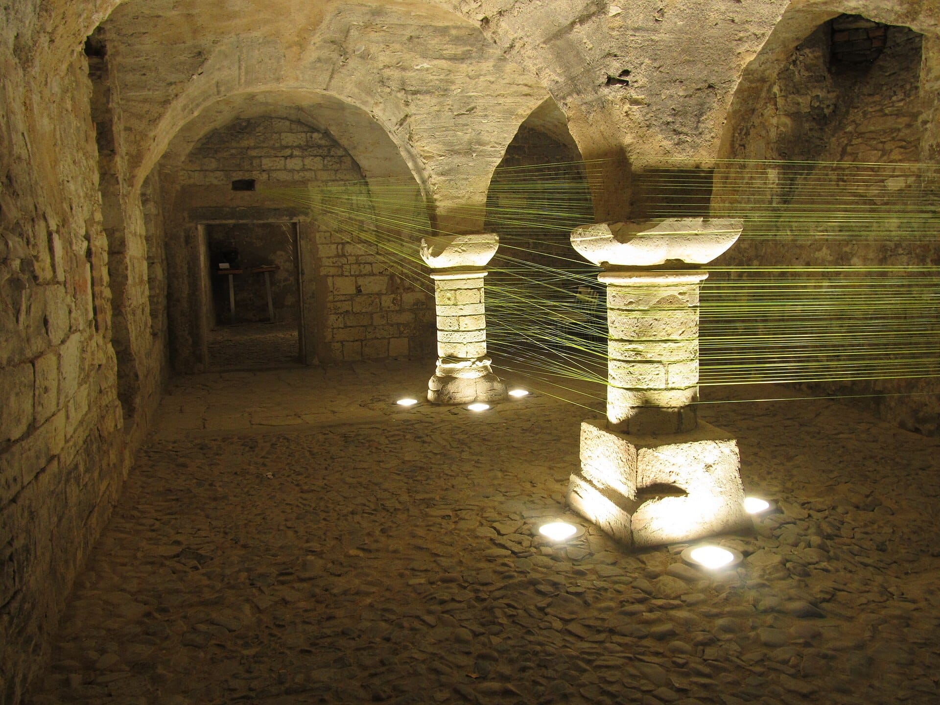 Steinbögen und Säulen, beleuchtet von warmem Licht im historischen Untergrund der Prager Altstadt, die mittelalterliche Architektur unter der Stadt zeigend.