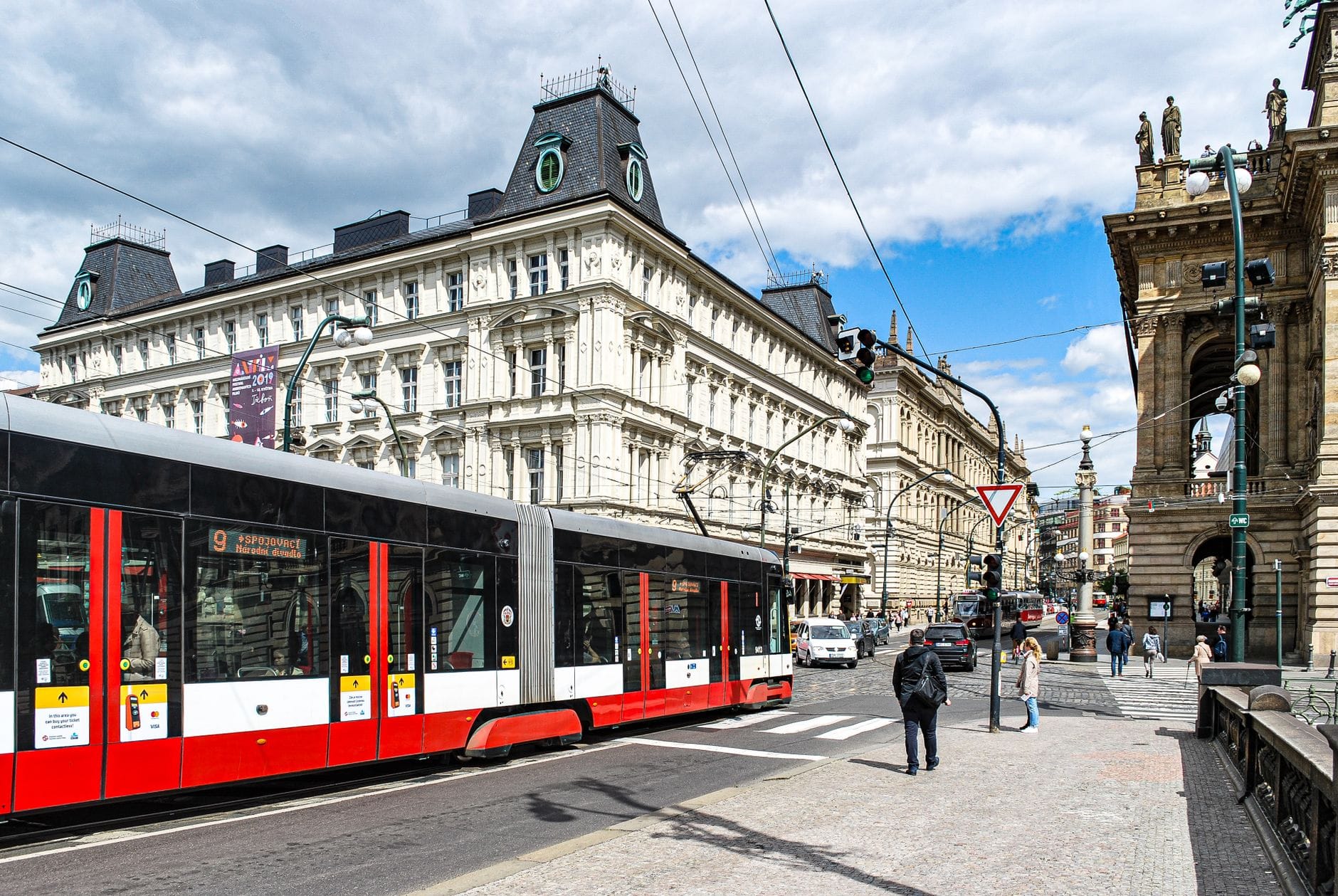 Modernong tram ng Prague na gumagalaw sa isang kalye ng lungsod na may mga dekoradong makasaysayang gusali at mga pedestryan sa likod.