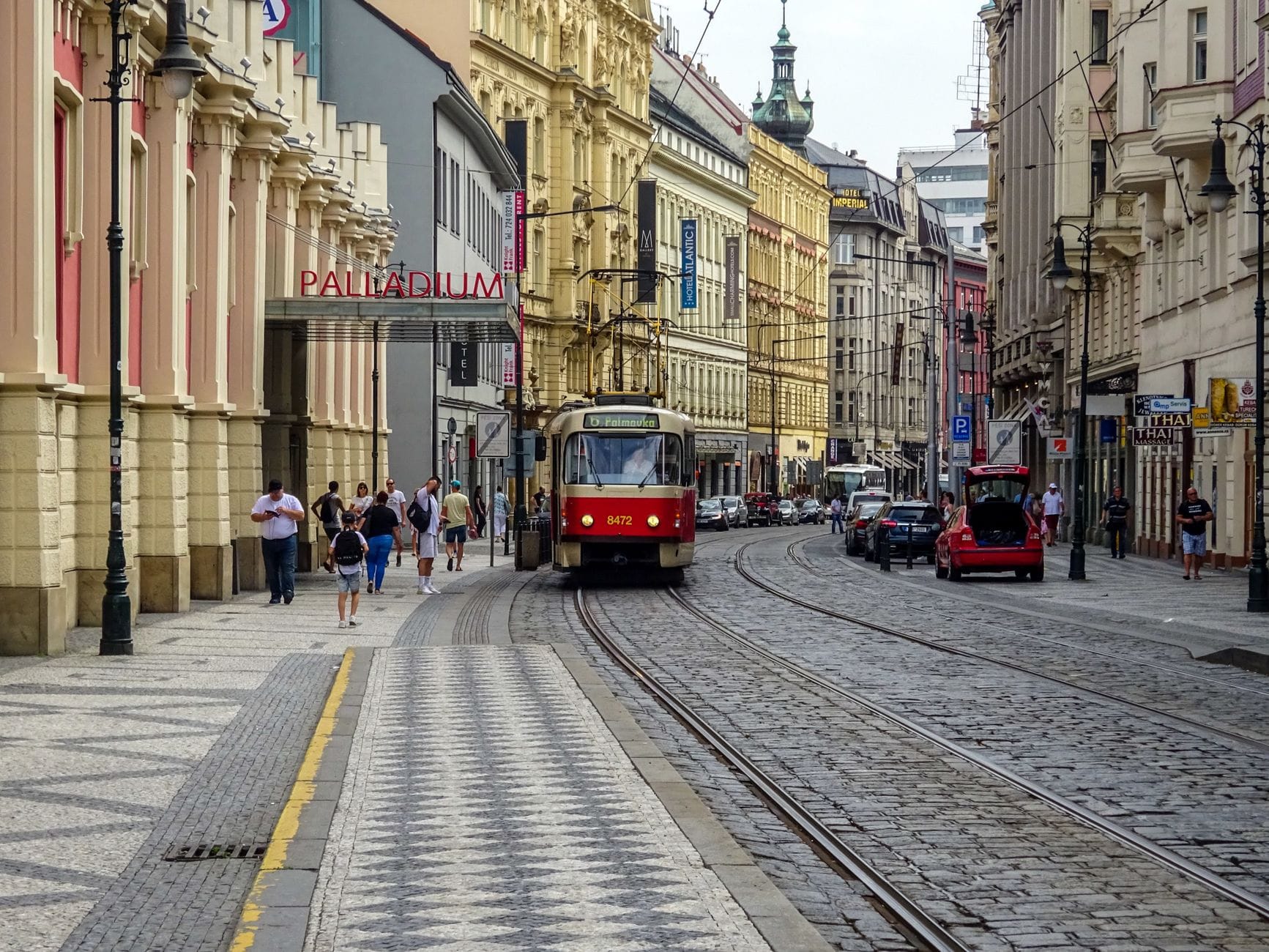 Eine belebte Straße in Prag mit Straßenbahnschienen, Fußgängern, Geschäften auf beiden Seiten und dem Eingang des Einkaufszentrums Palladium im Hintergrund.