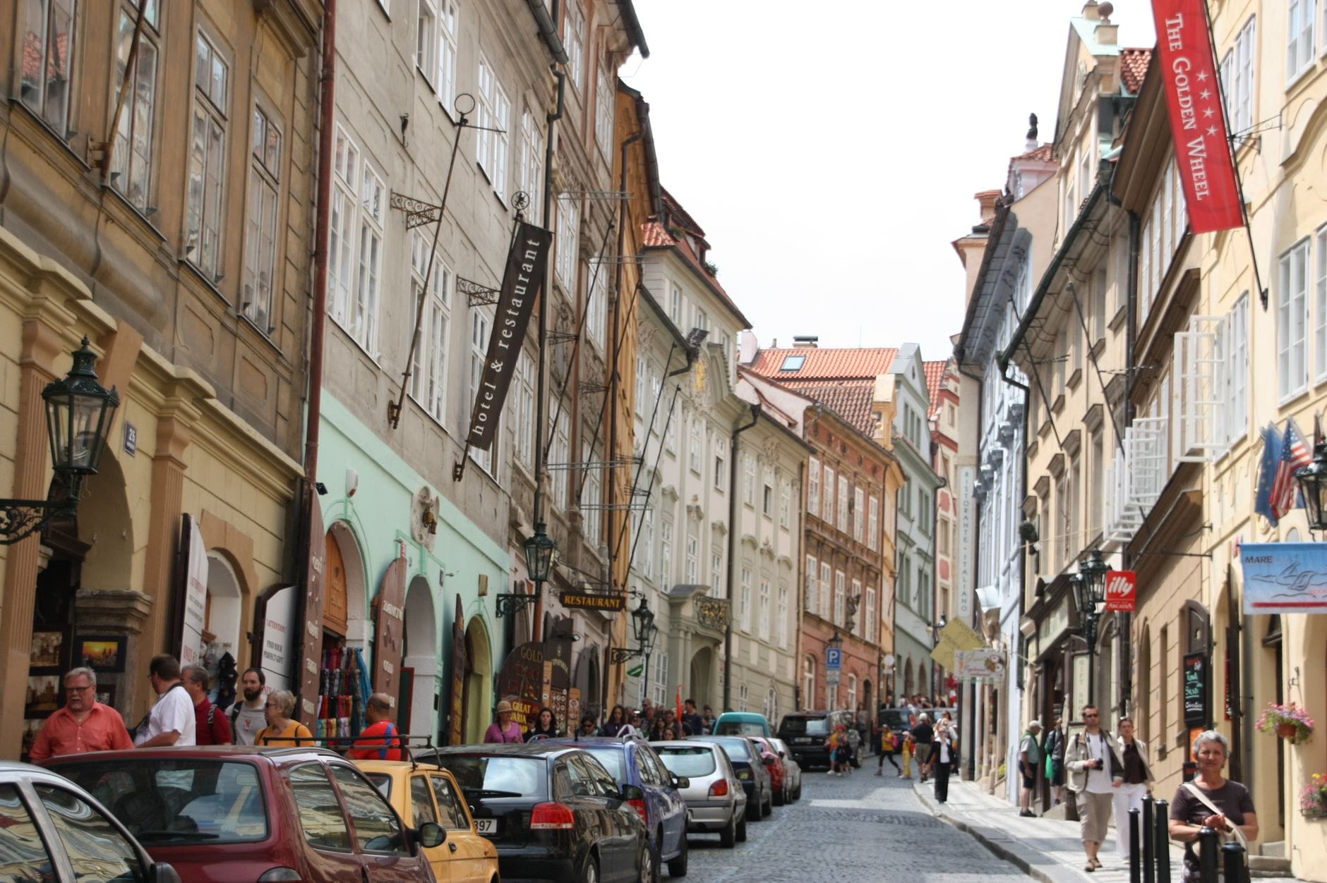 Belebte enge Straße im Zentrum von Prag mit Touristen, Autos und Geschäften, die einen typisch überfüllten Korridor auf der Route von der Altstadt zur Burg zeigt.
