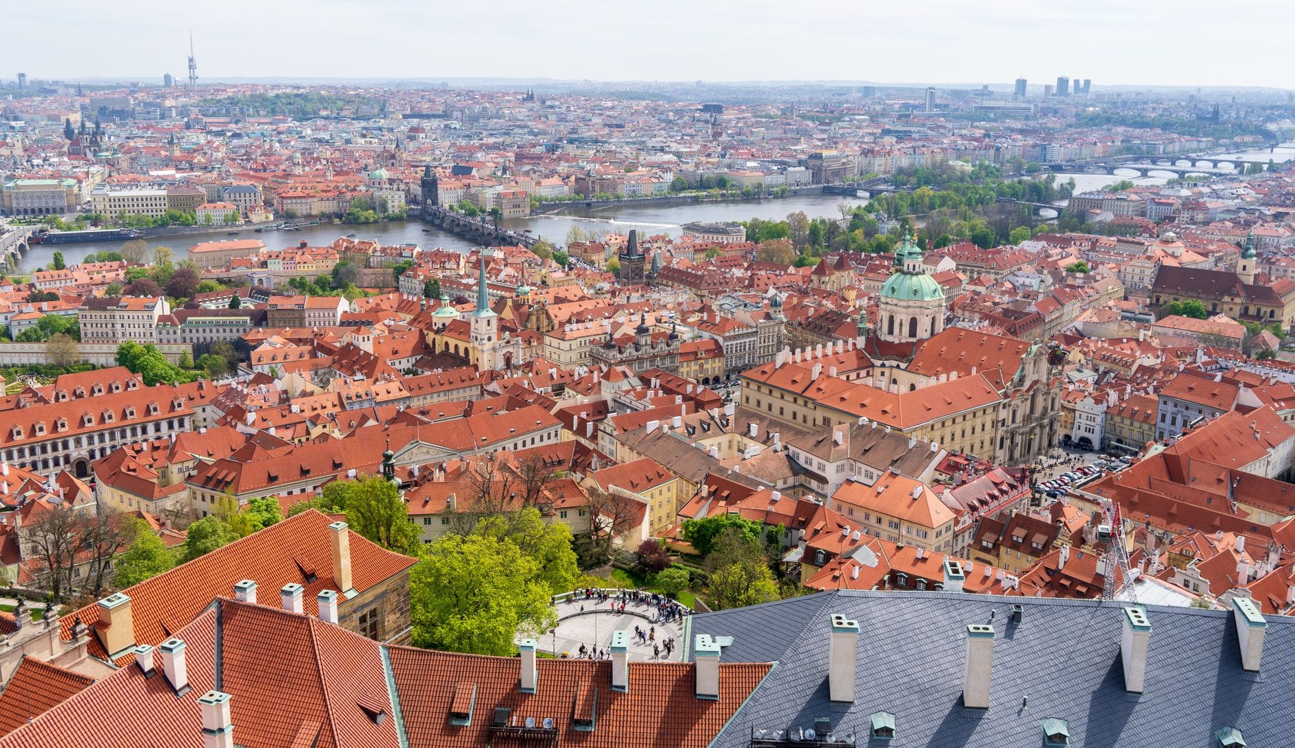 Weites Panorama über Prags historisches Zentrum mit roten Dächern, Kirchenkuppeln, der Moldau und berühmten Brücken unter einem hellen Himmel.