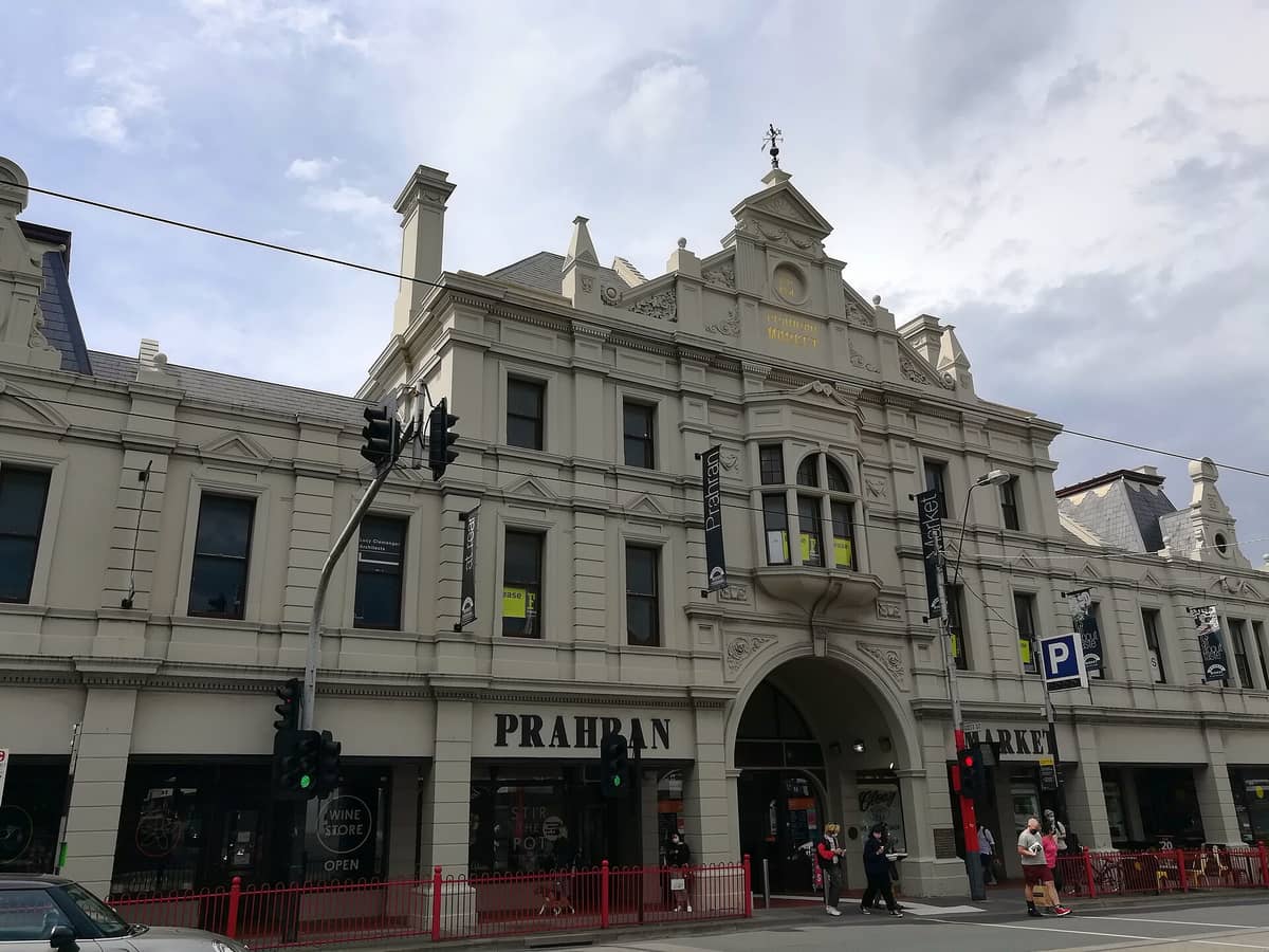 Weitwinklige Straßenansicht der historischen Fassade des Prahran Market in Melbourne, mit Passanten und dem gut sichtbaren Marktnamen über dem Eingang.