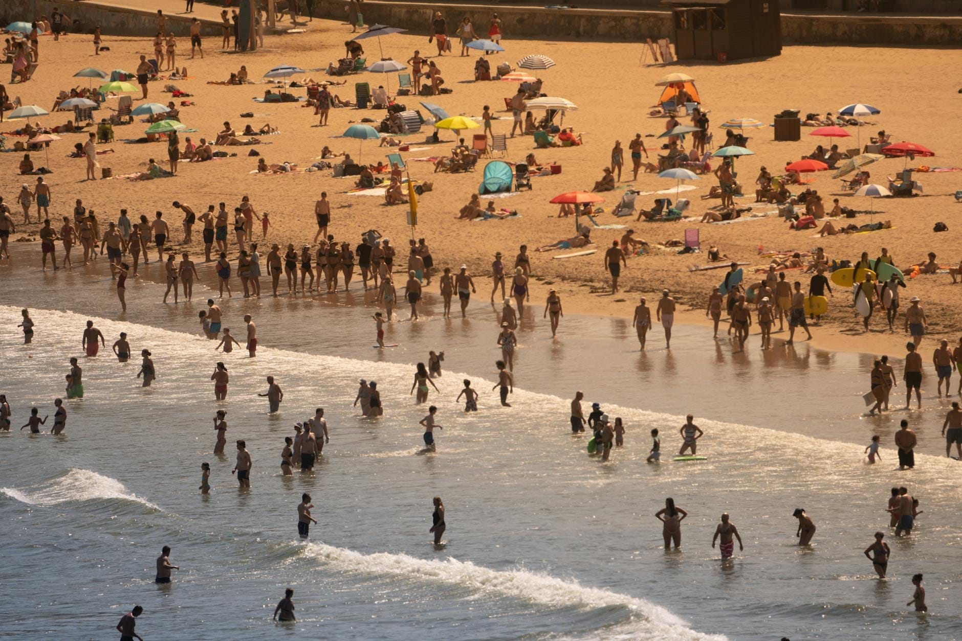 La Praia de Carcavelos affollata: persone che nuotano, prendono il sole sotto ombrelloni colorati e onde che si frangono sulla sabbia dorata.