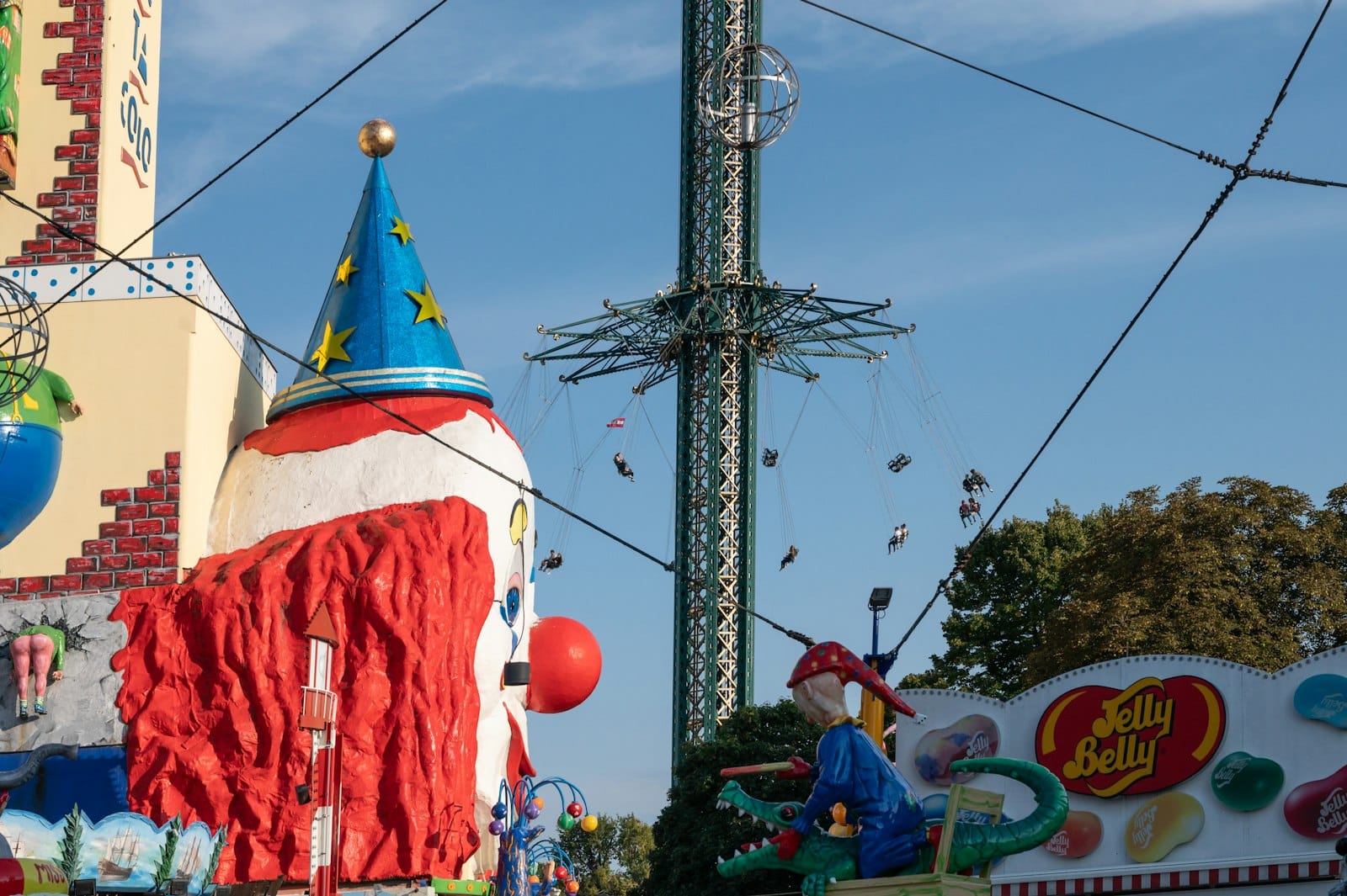 Buntes Treiben im Wiener Prater mit clownbuntem Gebäude, Drehturm und Jahrmarktdekoration unter klarem Himmel.